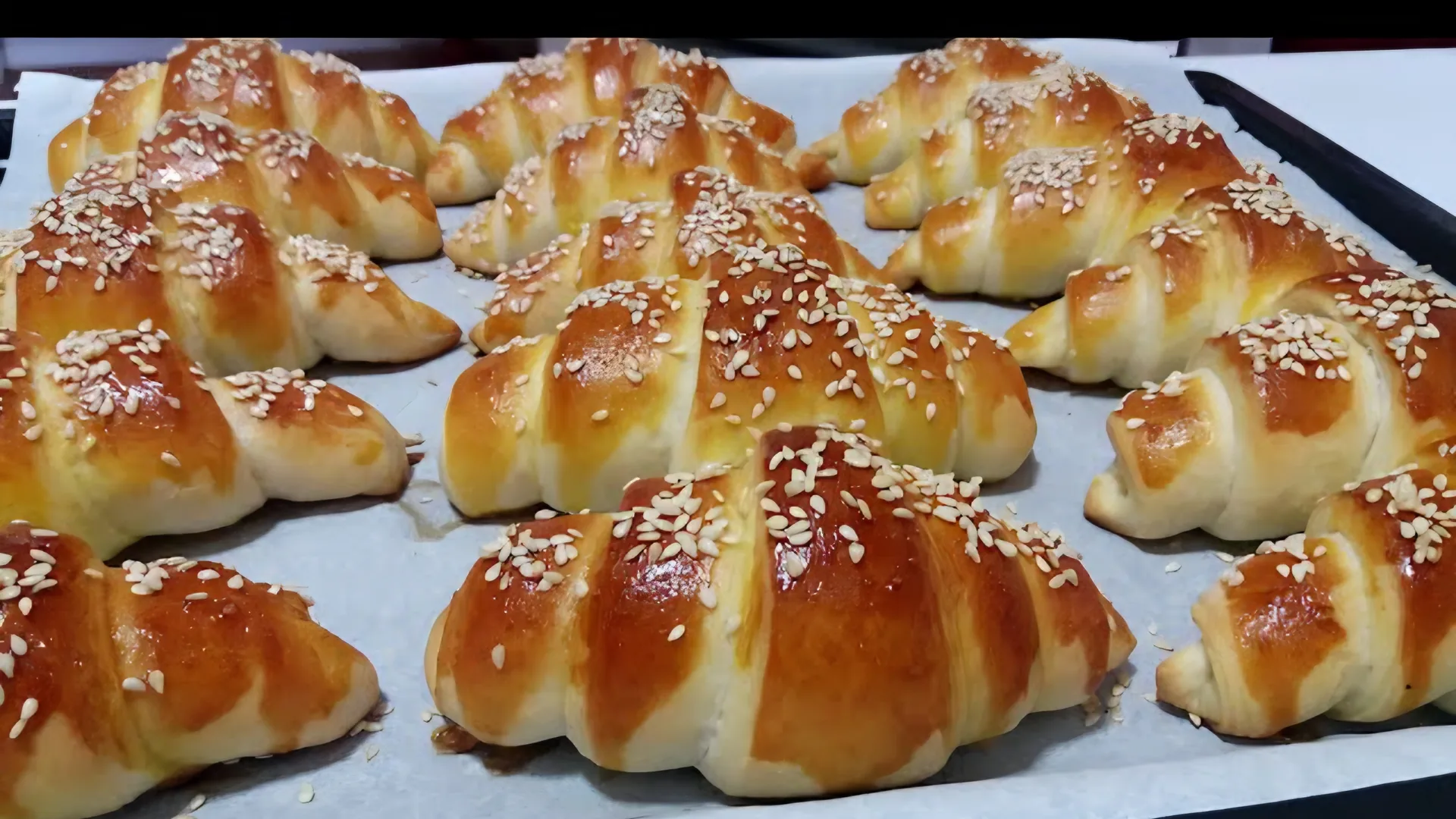 A tray of freshly baked kiflice, golden brown and sprinkled with sesame seeds.