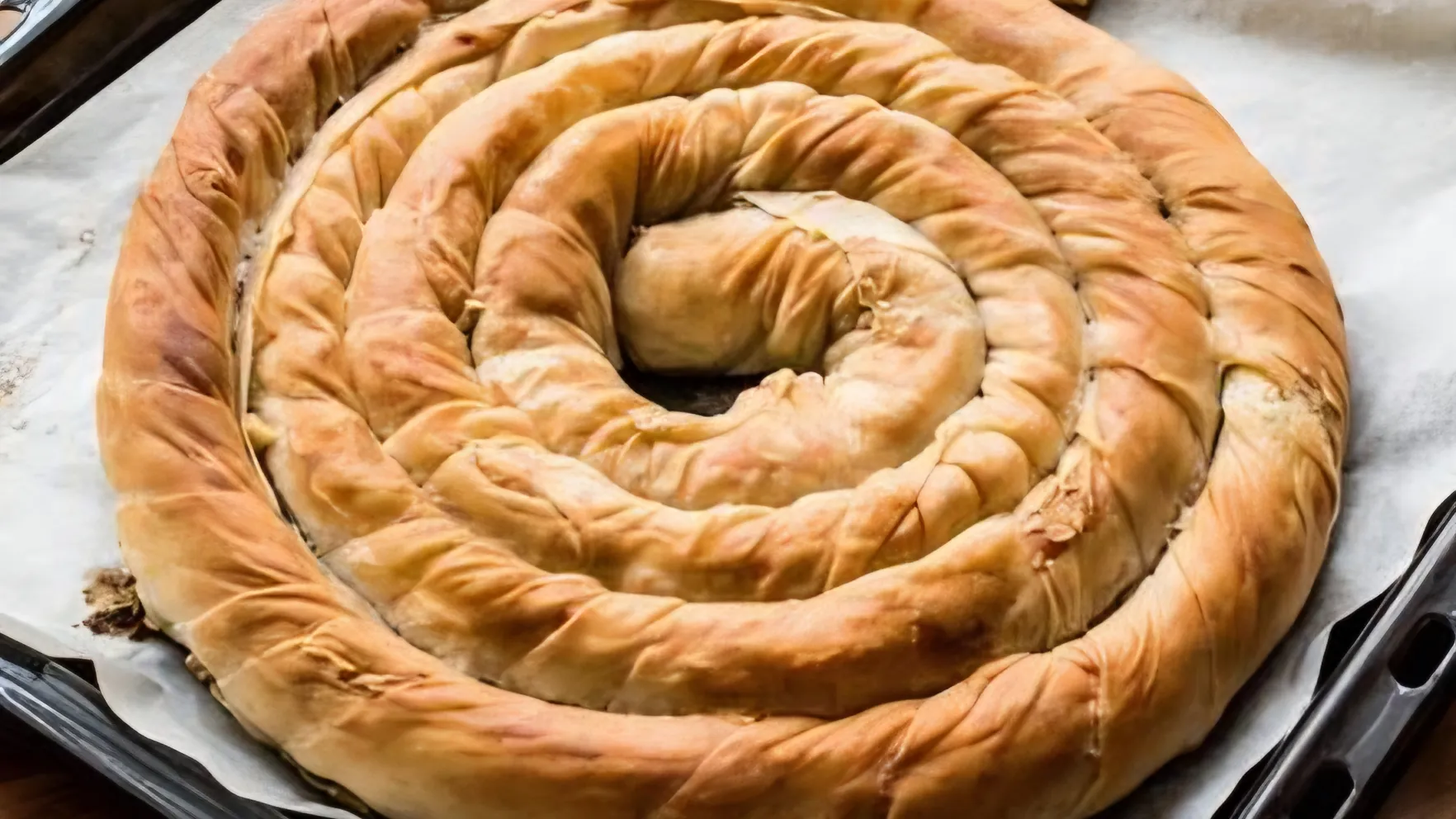 A large coiled pita, freshly baked and golden, on a parchment-lined baking tray.
